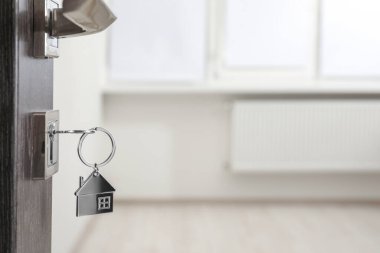İpotek ve gayrimenkul. Bulanık arkaplan için anahtar ve ev şekilli anahtarlık ile açık kapı, metin için boşluk