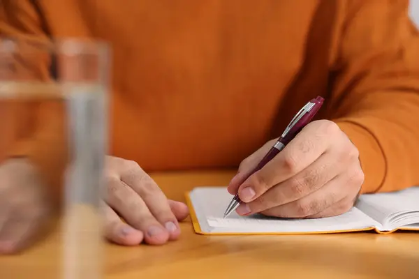 年轻人在木桌边的笔记本上写字 特写镜头 免版税图库照片