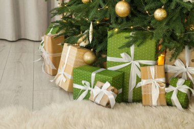 Noel ağacının altında bir sürü hediye kutusu süs süsleri ve oda ışıklarıyla süslenmiş.