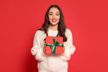 Kırmızı arka planda Noel hediyesi olan güzel genç bir kadın.