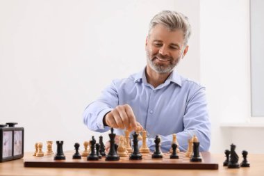 Happy man playing chess during tournament at table indoors clipart