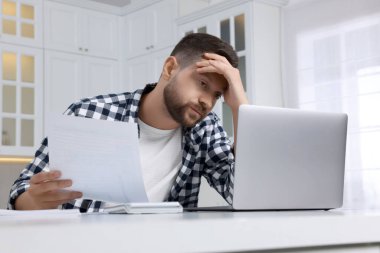 Bilgisayarlı adam mutfaktaki masada vergi işlerini yapıyor.