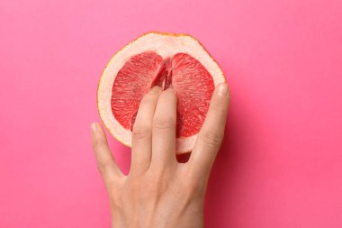Kadın pembe arka planda greyfurtun yarısına dokunuyor. Seks konsepti