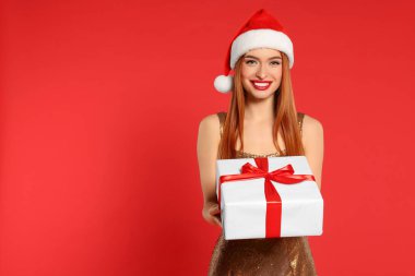 Noel Baba şapkalı genç kadın kırmızı arka planda Noel hediyesi, mesaj için yer var.
