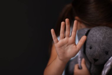 Çocuk istismarı. Oyuncak tavşanlı küçük kız karanlık arka planda hareketsiz duruyor, seçici odaklanma. Metin için boşluk