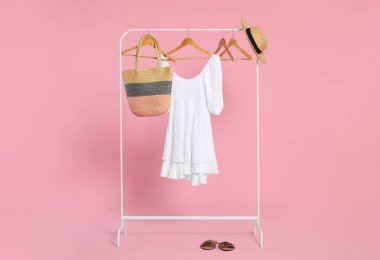 Aksesuarlı raflar ve pembe arka plandaki ahşap askılarda şık beyaz elbiseler.