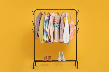 Süslü kadın kazaklarıyla ahşap askılar ve turuncu arka planda ayakkabılar.