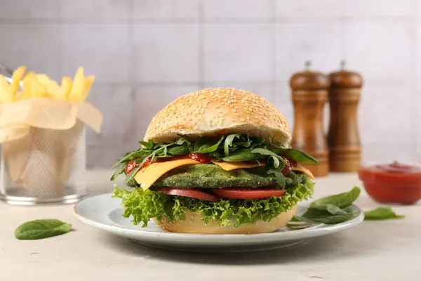 Tasty vegetarian burger with spinach cutlet, cheese and vegetables served on white table