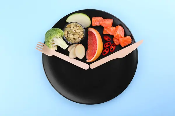 Metabolism. Plate with different food products and wooden cutlery on light blue background, top view