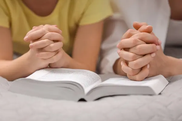 Girl and her godparent praying over Bible together indoors, closeup