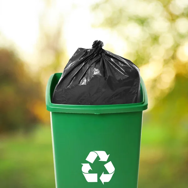 Waste bin with plastic bag full of garbage on blurred background