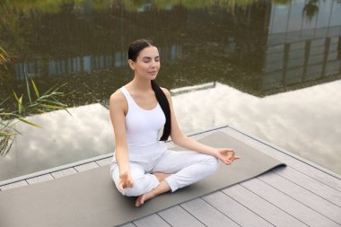 Güzel genç bir kadın yoga minderinde Padmasana egzersizi yapıyor. Lotus pozu