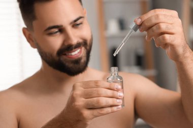 Elinde kozmetik serumu olan yakışıklı bir adam. Kapalı mekanda seçici bir odak.