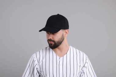 Açık gri arka planda şık siyah beysbol şapkalı bir adam.