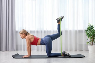 Spor yapan atletik bir kadın evde spor yaparken lastikli bant takıyor.