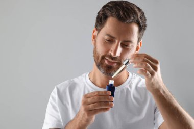 Açık gri arka planda kozmetik serumu olan yakışıklı bir adam. Metin için boşluk
