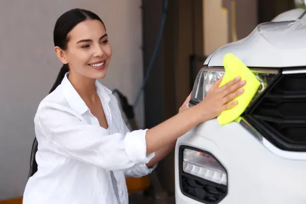 Happy woman cleaning headlight with rag at car wash