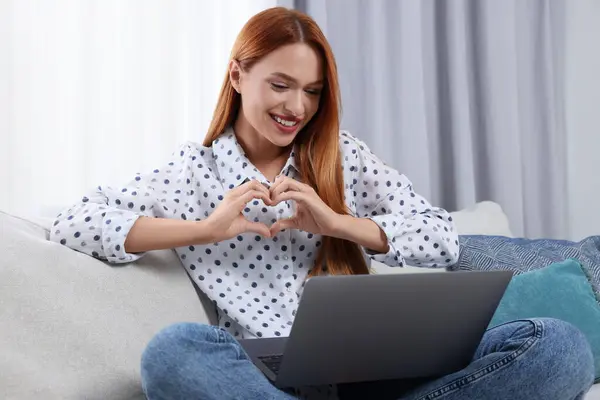 Woman making heart with hands during video chat via laptop at home. Long-distance relationship