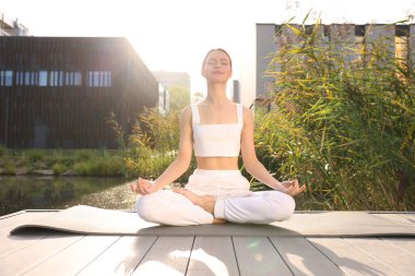 Güzel genç bir kadın yoga minderinde Padmasana egzersizi yapıyor. Lotus pozu