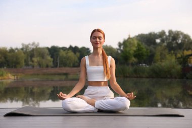 Güzel genç bir kadın yoga minderinde Padmasana egzersizi yapıyor. Lotus pozu