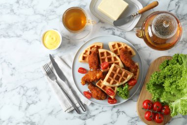 Beyaz mermer masada kızarmış tavuk, domates, marul ve çay ile servis edilen lezzetli Belçika waffleları.