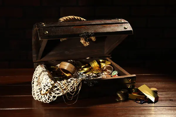 Treasure chest with net, gold bars, coins, jewelry and gemstones on wooden table