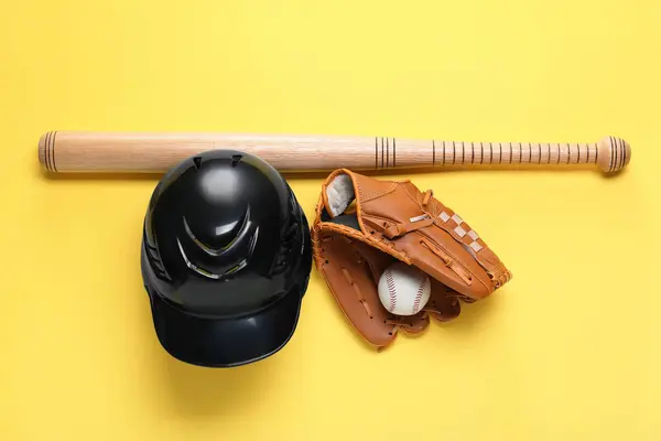 Baseball glove, bat, ball and batting helmet on yellow background, flat lay