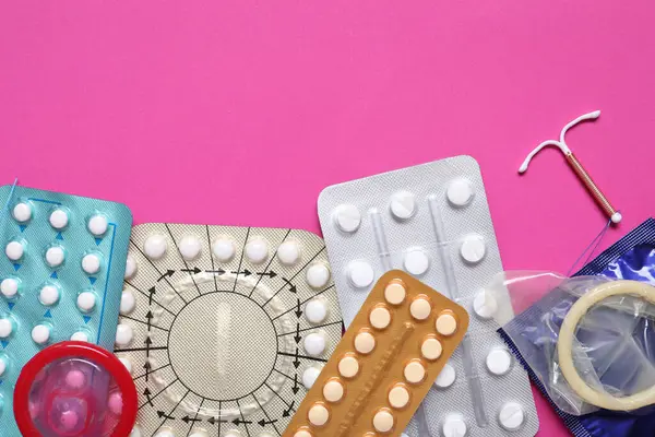Contraceptive pills, condoms and intrauterine device on pink background, flat lay with space for text. Different birth control methods
