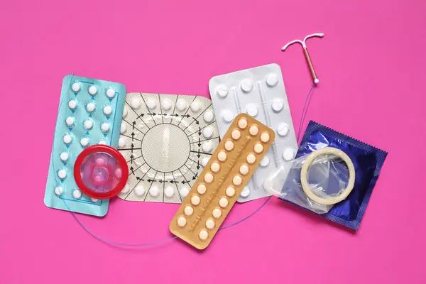 Contraceptive pills, condoms and intrauterine device on pink background, flat lay. Different birth control methods