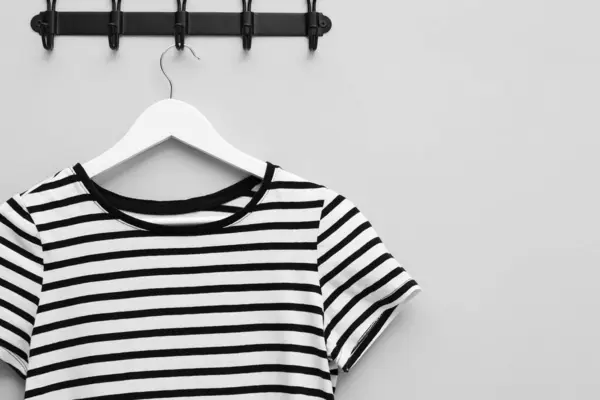 Hanger with striped T-shirt on light grey wall, space for text
