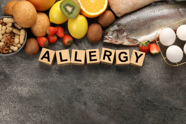 Food allergy. Different fresh products and wooden cubes on grey table, flat lay with space for text