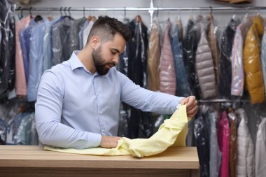 Kuru temizleme servisi. Kapalı mekanda tişört tutan bir işçi.