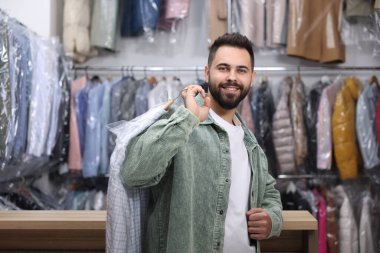 Kuru temizleme servisi. Kapalı mekanda plastik torba içinde gömlek tutan mutlu adam.