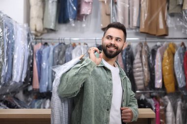 Kuru temizleme servisi. Kapalı mekanda plastik torba içinde gömlek tutan mutlu adam.