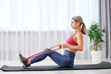 Formda bir kadın spor yapıyor. Evde lastik bantla.