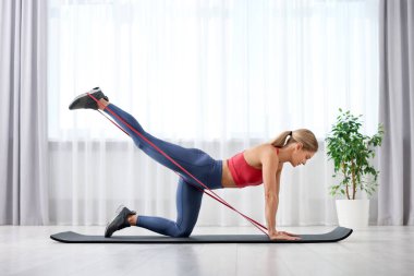 Spor yapan atletik bir kadın evde spor yaparken lastikli bant takıyor.