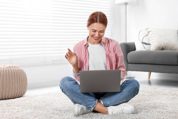 Женщина машет привет во время видео-чата через ноутбук дома