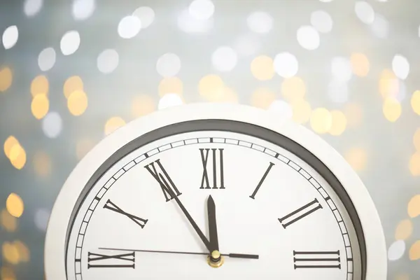 Clock showing five minutes until midnight on blurred background, closeup. New Year countdown