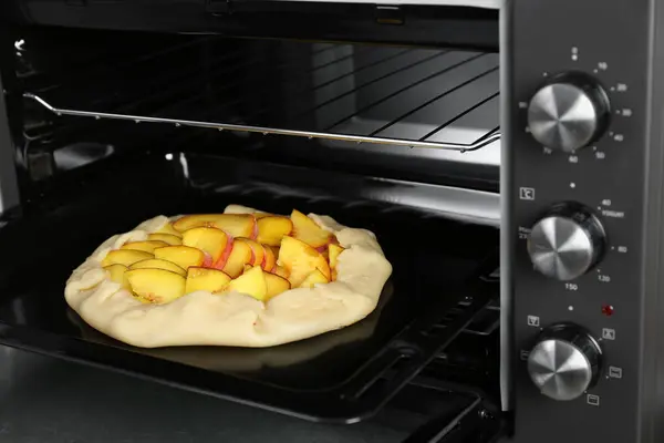 Open electric oven with uncooked pie on table in kitchen