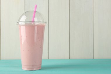 Beyaz ahşap duvara karşı açık mavi masada plastik bardakta nefis bir smoothie. Metin için boşluk