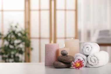 Spa kompozisyonu. Yanan mumlar, nilüfer çiçekleri, beyaz masa üzerinde taşlar ve havlular, yazı için yer