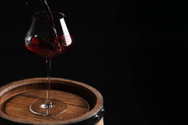 Siyah arkaplana karşı tahta fıçının üzerine kırmızı şarap dökmek. Metin için boşluk