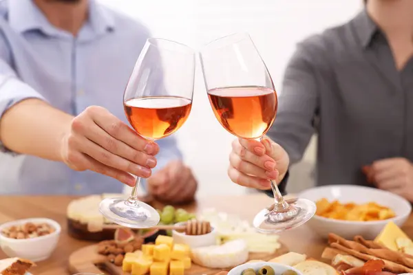 People clinking glasses with rose wine above wooden table indoors, closeup