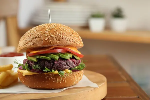 Tasty vegetarian burger with beet cutlet, cheese, avocado and tomato served on wooden table, closeup. Space for text