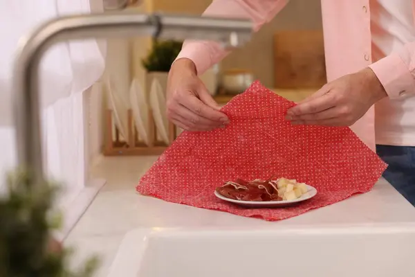 Man packing ham and cheese into beeswax food wrap at white countertop in kitchen, closeup