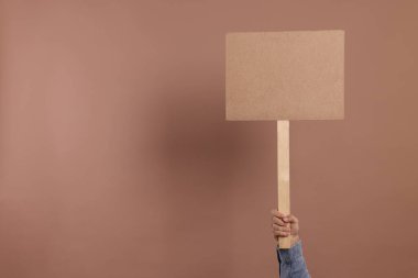 Kahverengi arka planda boş tabela tutan adam, yakın plan. Metin için boşluk