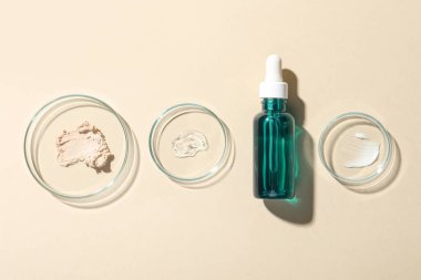 Bir şişe kozmetik serumu ve bej arka planda örnekler içeren petri kapları.