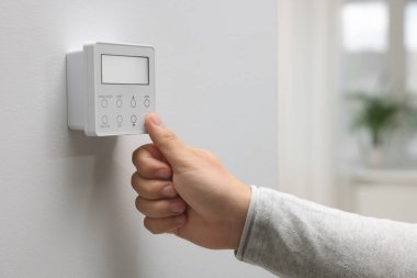 Beyaz duvardaki termostatı ayarlayan kadın, yakın plan. Akıllı ev sistemi