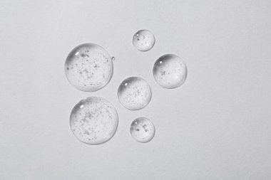 Beyaz arka planda kozmetik serumu damlaları, üst görünüm