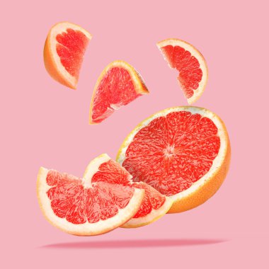 Pembe arka plana düşen greyfurt parçaları.